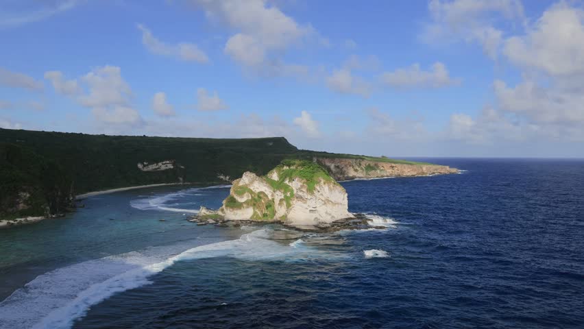 Saipan features turquoise waters, white sandy beaches, lush cliffs, coral reefs, and scenic caves. The clear blue sky, fluffy clouds, and crystal-clear ocean create a breathtaking tropical paradise