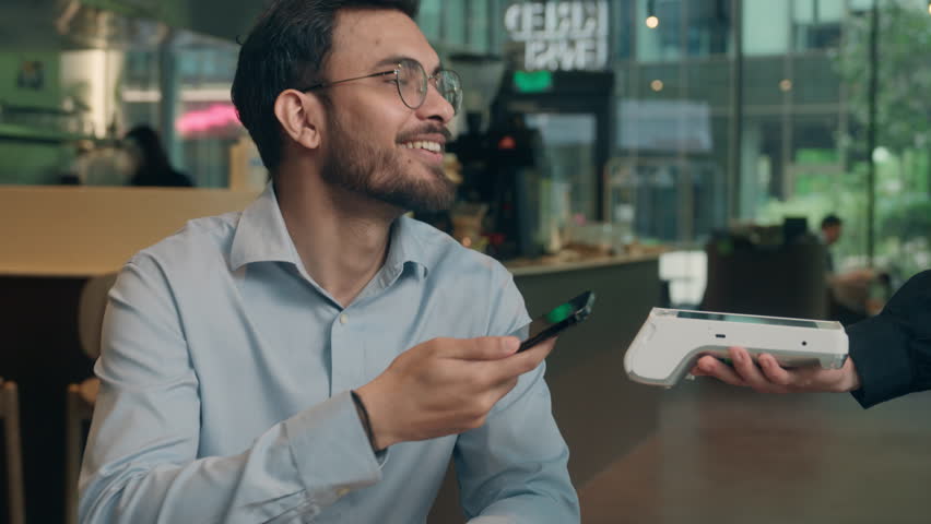 Waiter serving visitor in cafe Indian man guy male customer buyer client businessman coffee pay smartphone wifi scan contactless NFC payment online technology mobile phone credit card bank terminal
