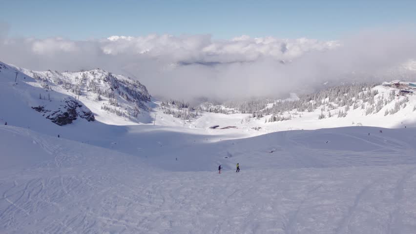 Downhill skiers with mountain vista, aerial footage, ski mountain, sunny day, winter, ski hill, Whistler BC. 5.4K 24FPS