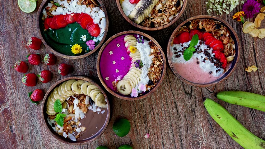 Healthy Bowls of Pretty Smoothie with Fresh Fruits and Juicy Berries on Wood Table Close Up. Top Shot on Dish of Plant Milk and Mango Puree. Toppings of Bright Strawberries with Raw Banana and Flowers