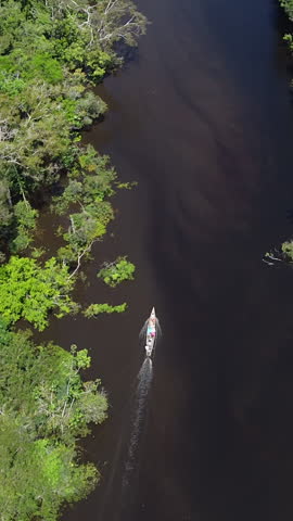 Vertical - People On Boat Ride On Amazon River Through Lush Rainforest In Peru. aerial topdown, tracking shot