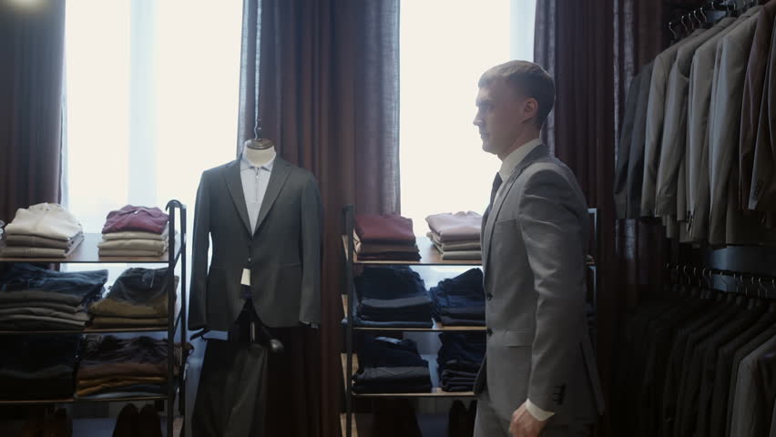 Professional businessman rotating slowly, admiring tailored suit and refined appearance while examining reflection in upscale clothing store mirror