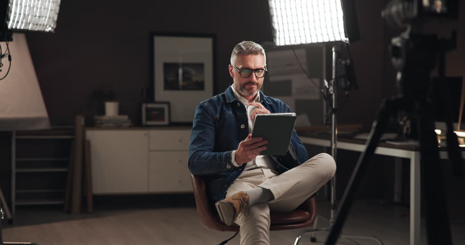 Tablet, filming and man on set reading script for documentary interview or podcast episode. Digital technology, research and male journalist recording for online live streaming show with lights.