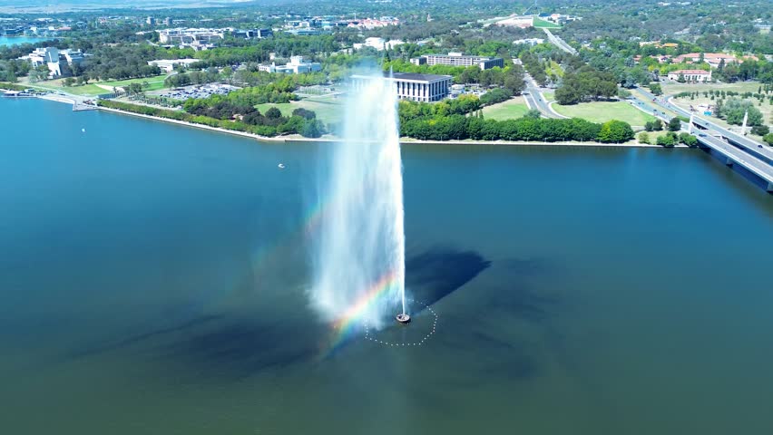 Drone aerial landscape of rainbow reflection within water fountain jets Captain Cook Memorial landmark with bridge overpass in Lake Burley Griffin Canberra ACT Australia travel tourism attraction