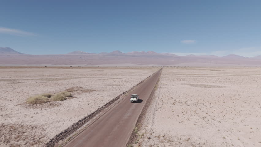 Drone shot flying over the dry sand desert mountains in San Pedro de Atacama Chile South America on a blue sky day with a white truck driving along near Mars Valley and Valley de la Luna LOG