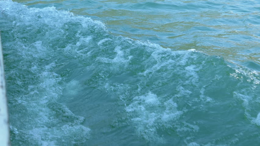 Close-up of foamy water trailing a boat, creating dynamic patterns and textures against a serene turquoise backdrop.