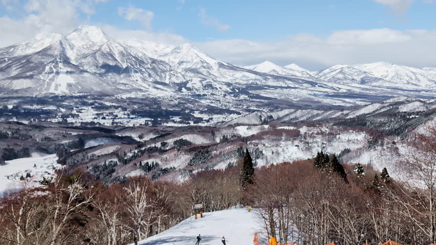 Skiers descending narrow slope with blue sky.Madarao Japan