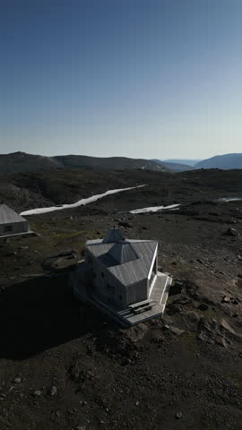 Vertical aerial shot panning around showing Rabothytta cabin, situated on the edge of Okstindbreen glacier, with views of the Okstindan mountain range in the distance. Korgen, Norway