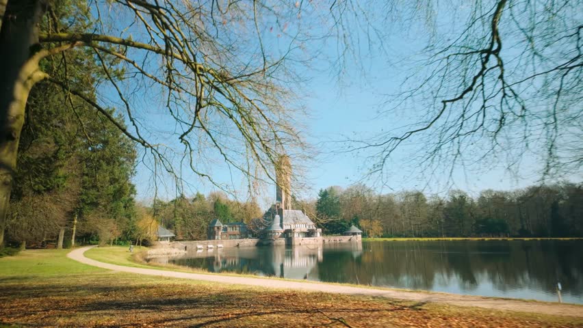 The iconic Jachthuis Sint Hubertus, a historic hunting lodge, framed by tree branches under a bright blue sky in Hoge Veluwe National Park, Netherlands.