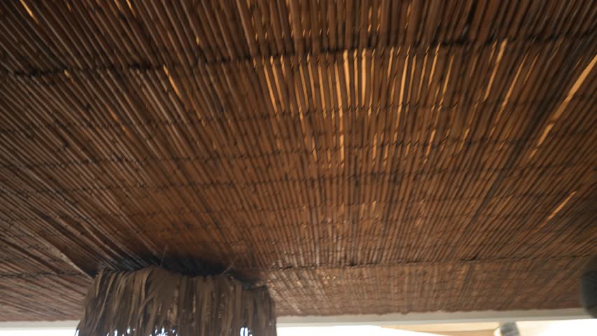 A bamboo ceiling in a beach venue features a decorative element made of dried palm leaves in a boho style, enhancing the tropical ambiance.