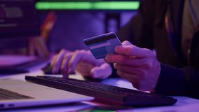Close up shot of hands of anonymous hacker stealing users data holding credit card by laptop in neon room - Powered by Shutterstock - Get 15% off with code: PIKWIZARD15