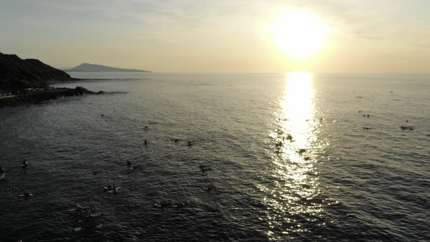 Surfers floating on shimmering ocean waters at sunset, seascape, backlight, Plage de Lafitenia beach, France. Aerial forward, copy space