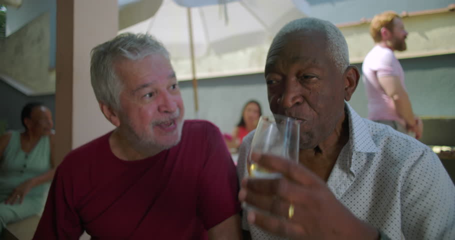 Two elderly friends smiling and drinking beer at a backyard barbecue, sharing joyful moments and celebrating friendship during a relaxed and lively outdoor gathering