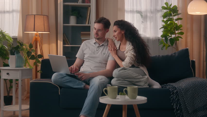 Smiling happy multiracial couple multiethnic Caucasian man male guy husband boyfriend with Hispanic Latina woman female girl wife girlfriend shopping computer together talking discuss laptop at home