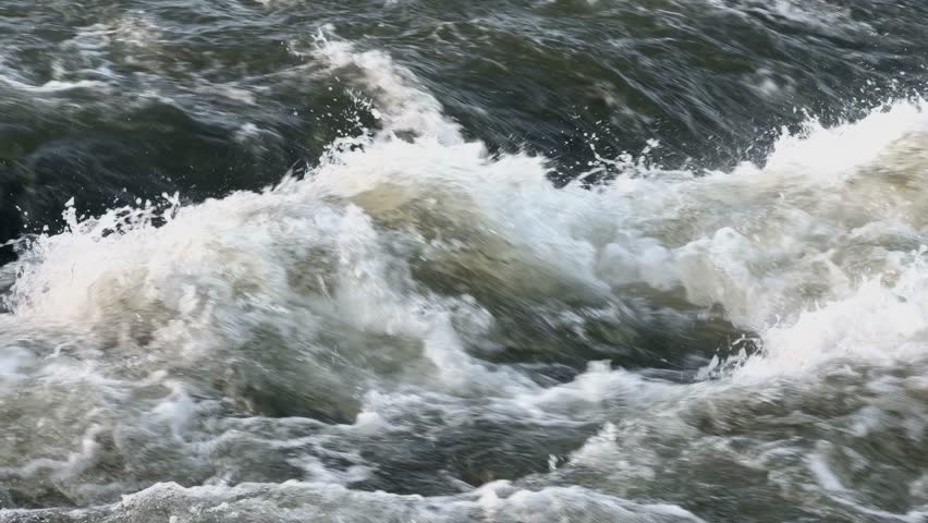Dark green river water flows rapidly, churning and creating white, foamy waves.  Perfect for projects about nature, environment, or travel. Slow-motion recording at half speed. (Ultra HD)