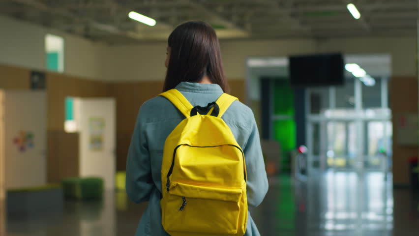 Unrecognizable woman walking going to class Caucasian female teenager girl student teenage pupil in school corridor hall lesson academy education with yellow schoolbag learn indoor schooling exams