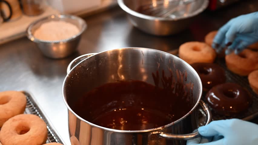 Golden donuts fresh from the fryer, ready for their final touch, a rich, glossy chocolate glaze that makes them irresistible