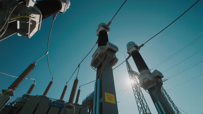 High-voltage electrical substation with insulators and power lines against blue sky