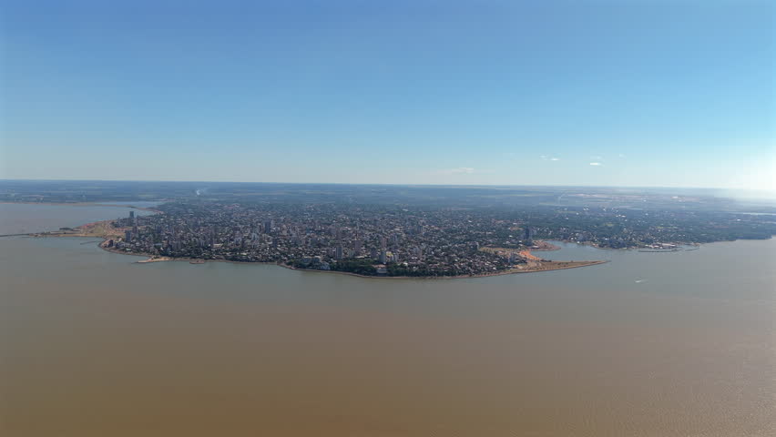 A wide-angle aerial view of the city of Posadas, located in Misiones Province, Argentina, with the Paraná River flowing on the left side.
