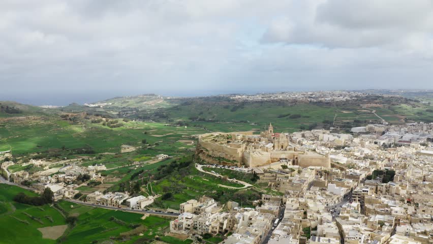 Very wide orbiting shot of a hill in Gozo, with Citadella de Victoria, Malta, drone