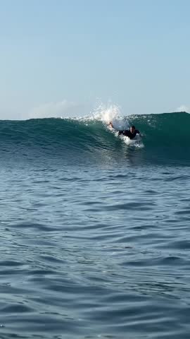 Surfer ridding a blue wave and making a spray in Indian Ocean.Surfing action shot. Wide angle view.Vertical video