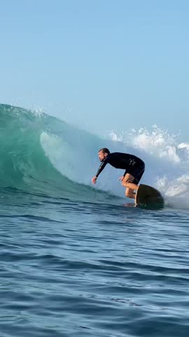 Surfer ridding a blue wave and making a spray in Indian Ocean.Surfing action shot. Wide angle view.Vertical video