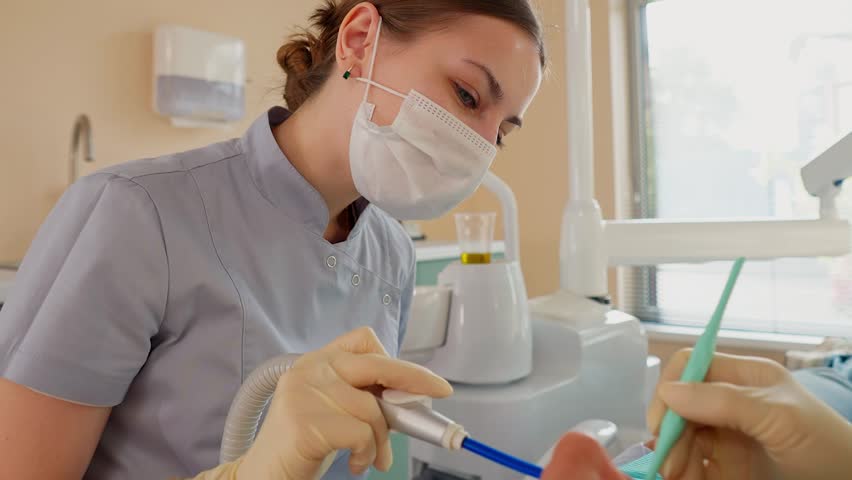 Blonde Woman Dentist with Assistant Treat Teeth of Female Patient with Special Instrument. Treatment of Caries and Plaque in Dental Clinic. Concept of Medicine and Healthcare. Slow Motion.