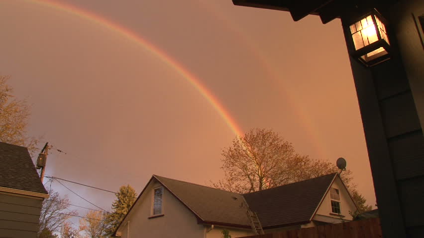 Double rainbow appears over houses in neighborhood on rainy, Spring evening.