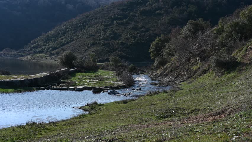 A tranquil lake surrounded by rolling hills, with a stone pathway leading across the water, reflecting sunlight on a peaceful day.  
