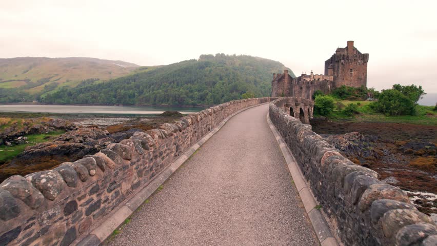 Beautiful Drone Along Stone Bridge Leading to Eilean Donan Castle Scotland. Water Moat Around Medieval Stone Fortress Morning.