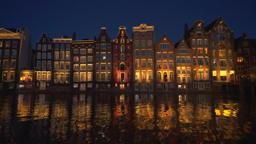 Amsterdam Damrak Canal Dancing Houses Lit Up at Night. Reflective Water Wide Low Angle 4K High Quality Color Corrected..