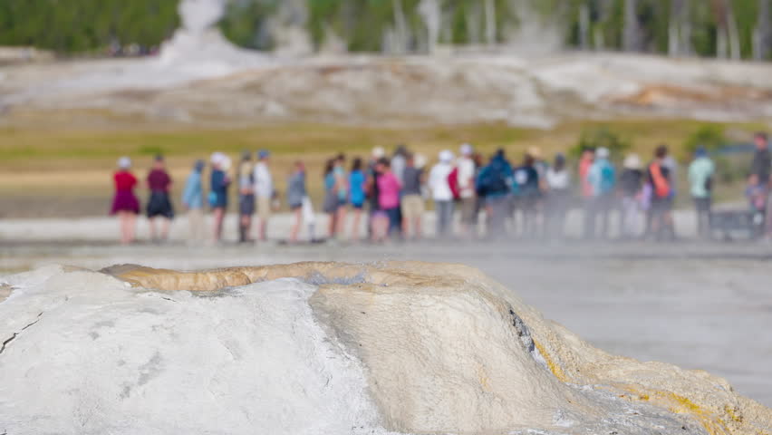 A bubbling geyser releases steaming vapors while crowds gather in Yellowstone National Park to witness its powerful geothermal activity.