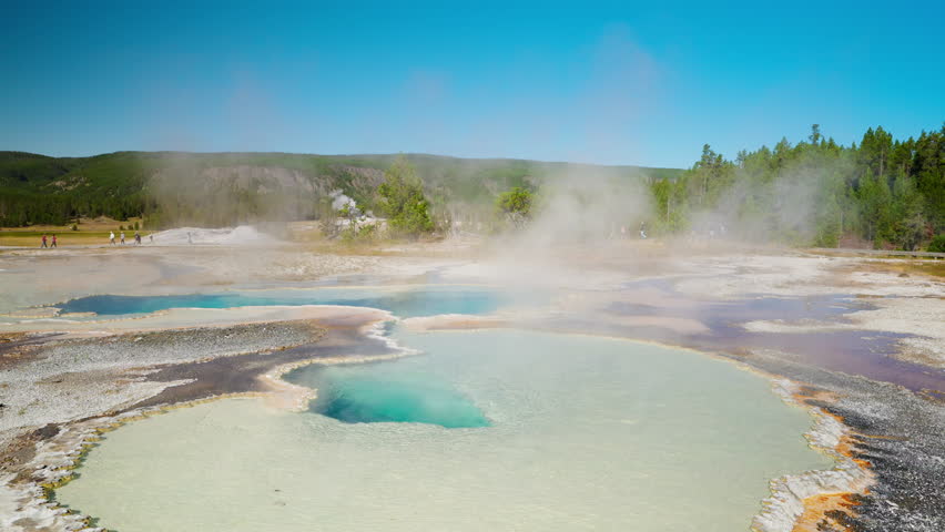Yellowstone’s vibrant hot spring bubbles and steams, its vivid colors contrasting with the warm summer air and natural surroundings.