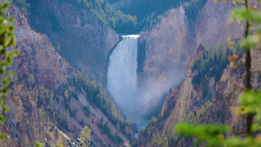 Lower Falls in Yellowstone cascades dramatically into a beautiful mountain valley, surrounded by lush forests and the winding river, creating a breathtaking natural vista.