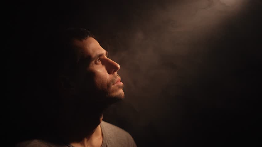 Man gazes upward as divine light pierces surrounding darkness