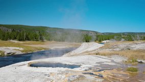 On a summer day in Yellowstone, geysers erupt alongside a flowing river that winds through lush forests, highlighting the park’s diverse natural beauty. - Powered by Shutterstock - Get 15% off with code: PIKWIZARD15