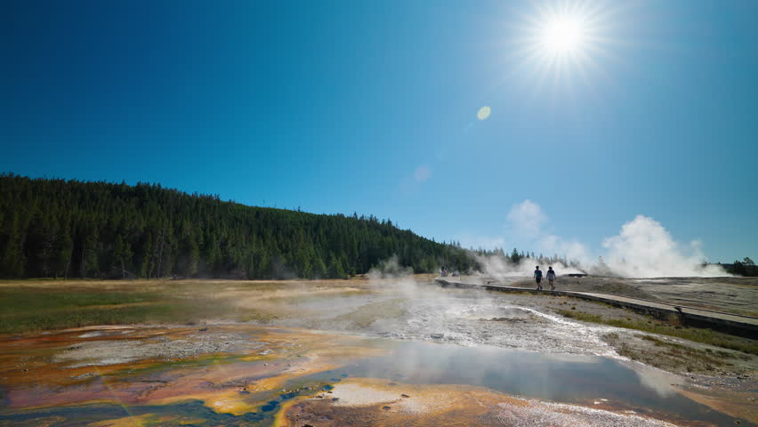 Yellowstone National Park visitors explore steaming hot springs and erupting geysers, walking through the geothermal wonderland on a warm summer day.