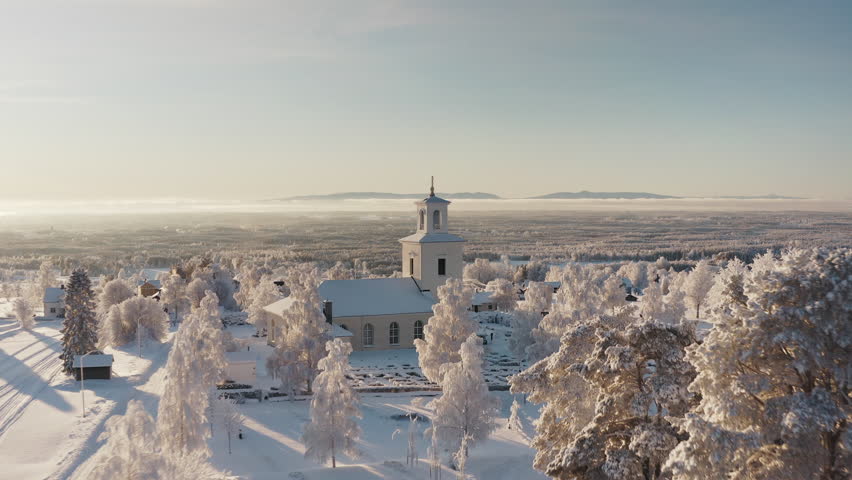 Snowy sunny droneshot towards church in Jämtland sweden, trees in forground