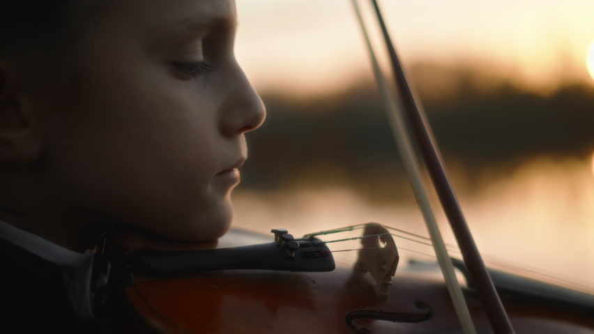 Close-up, girl playing violin on the background of a river at sunset