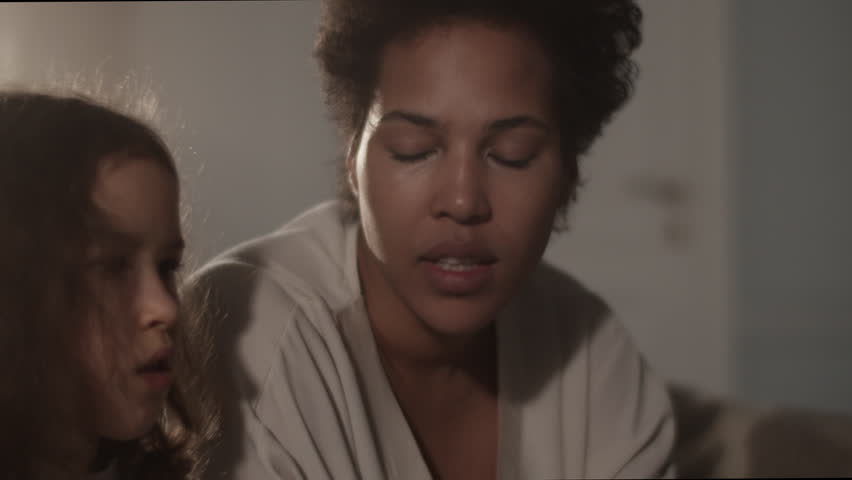 Black mother teaching daughter music from book with syllables