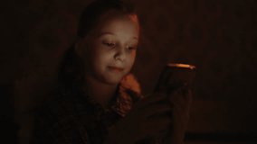 Beautiful young girl with striking blue eyes using smartphone in dimly lit room at night, illuminated by soft glow of screen, radiating happiness and enjoyment. Cute child enjoying mobile apps, games. - Powered by Shutterstock - Get 15% off with code: PIKWIZARD15