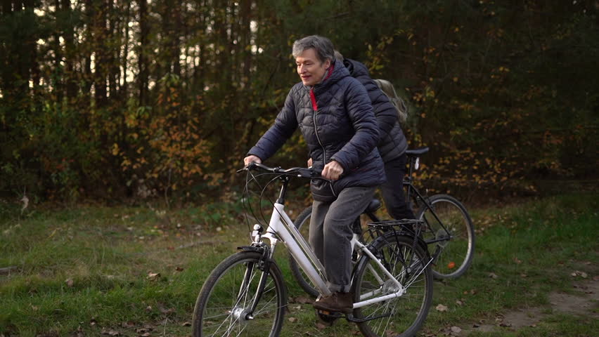 Couple of pensioners riding a bicycle in autumn on an autumn day. People over 60, aging youthfully. High quality FullHD footage