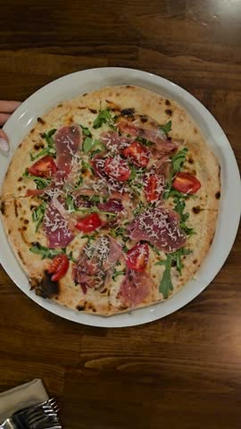 Freshly cooked Italian pizza with melted mozzarella cheese, smoked pork bacon hams and arugula leaves toppings in a plate on white table.
