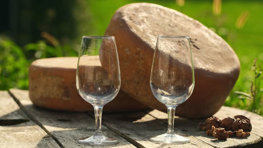 Pouring white wine into two glasses with delicious Ossau-Iraty cheese wheels in the background. Ossau-Iraty is a Basque cheese made from sheep