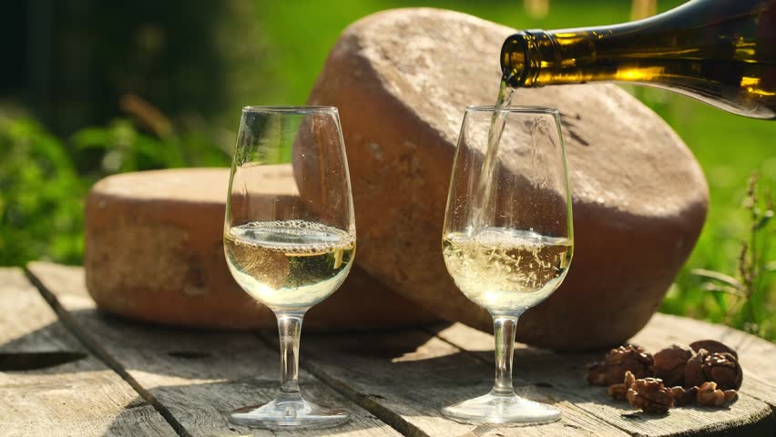 Pouring white wine into two glasses with delicious Ossau-Iraty cheese wheels in the background. Ossau-Iraty is a Basque cheese made from sheep's milk. 