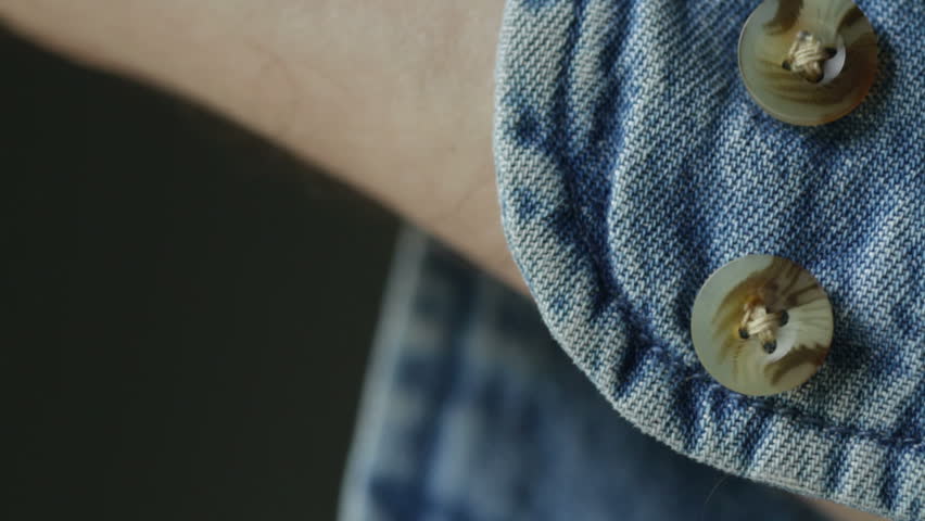 Close shot of hand doing up the button on the cuff of a denim shirt. Recorded
