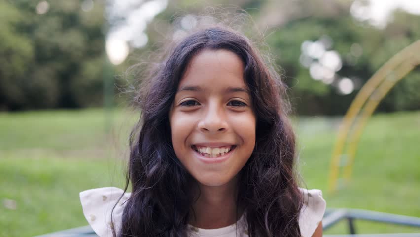 Happy latin female child smiling on camera with kid park on background. Childhood life concept