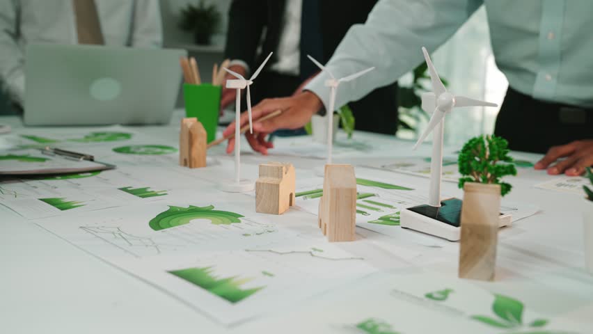 A diverse business team collaborates on renewable energy strategies, showcasing wind turbine models and green plants during an engaging planning session in a modern office. SACTR - Powered by Shutterstock - Get 15% off with code: PIKWIZARD15