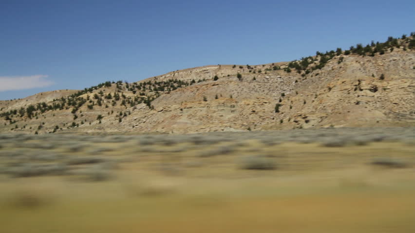 Driving view of Wyoming landscape with scrubland in foreground and rocky