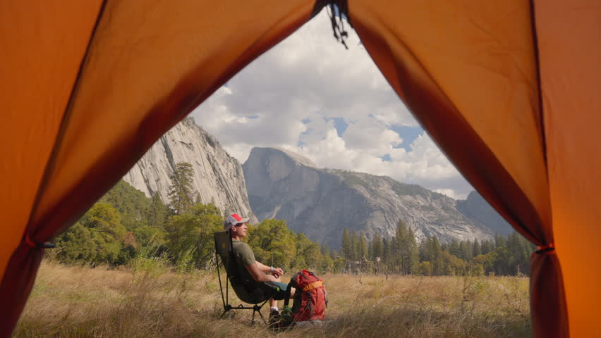This picturesque camping scene set in Yosemite National Park captures the breathtaking beauty of the mountain vistas, a welcoming tent, and a backpacker peacefully immersed in natures splendor